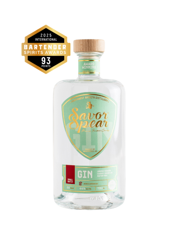 A bottle of Savor Spear Gin by Northwest Spirits is shown with a clear, modern design. The label is mint green with gold and white accents, featuring the brand name prominently in gold script. The bottle is sealed with a natural wood cap. A badge on the upper left highlights a gold medal from the 2025 International Bartender Spirits Awards, indicating the gin received 93 points.