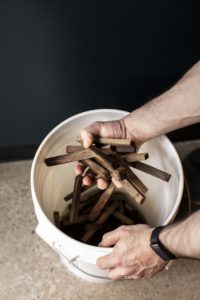 A man is holding a group of about 10 pieces of wood oak staves over a white bucket