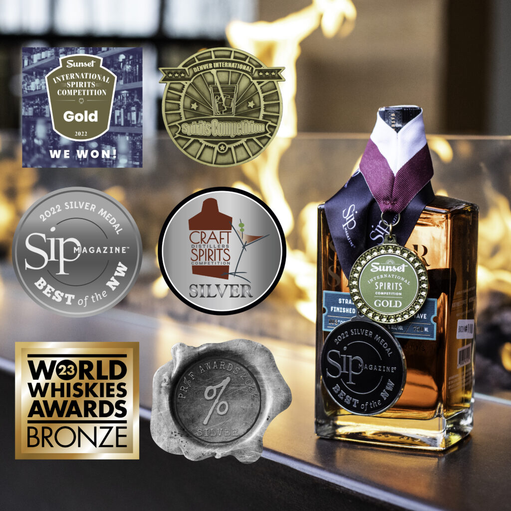 A bottle of Savor Spear Bourbon sitting in front of an outdoor fireplace with 2 medals around the neck of the bottle. There are also 6 icons on the photo next to the bottle that represent all of the awards the whiskey has won. 