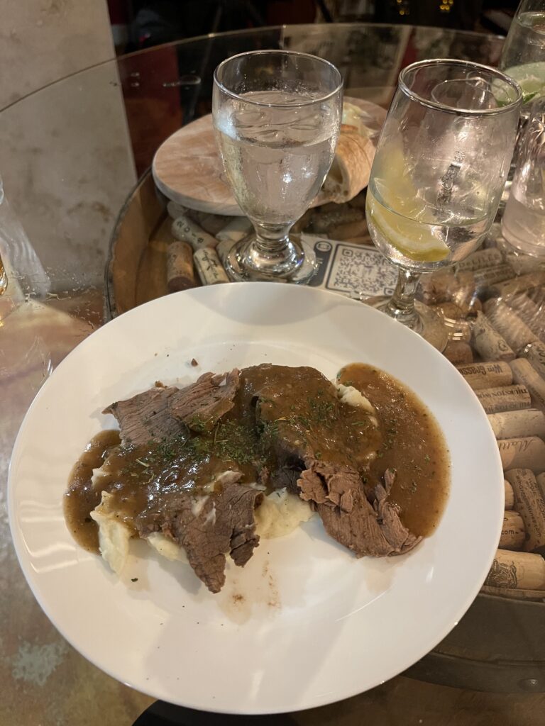 Photo of a plate of Rump Roast sliced beef sitting atop a bed of mashed potatoes, topped with gravy and sprinkled with parsley.