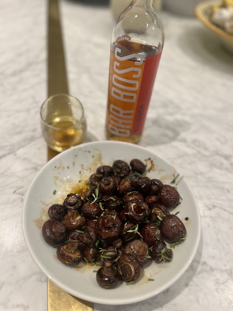A plate of yummy baked mushrooms and a glass of whiskey behind it