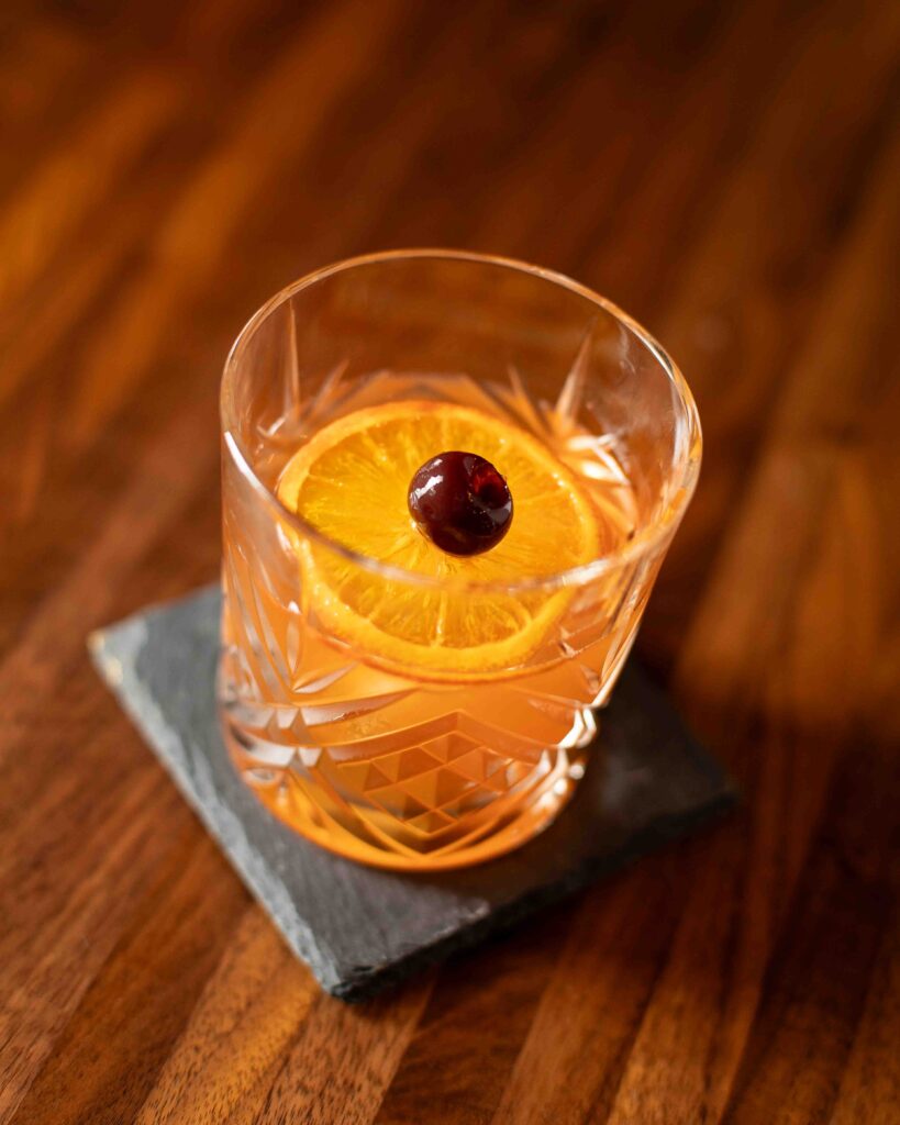 Northwest Spirits Old Fashioned in a crystal glass, garnished with an orange wheel and cherry.