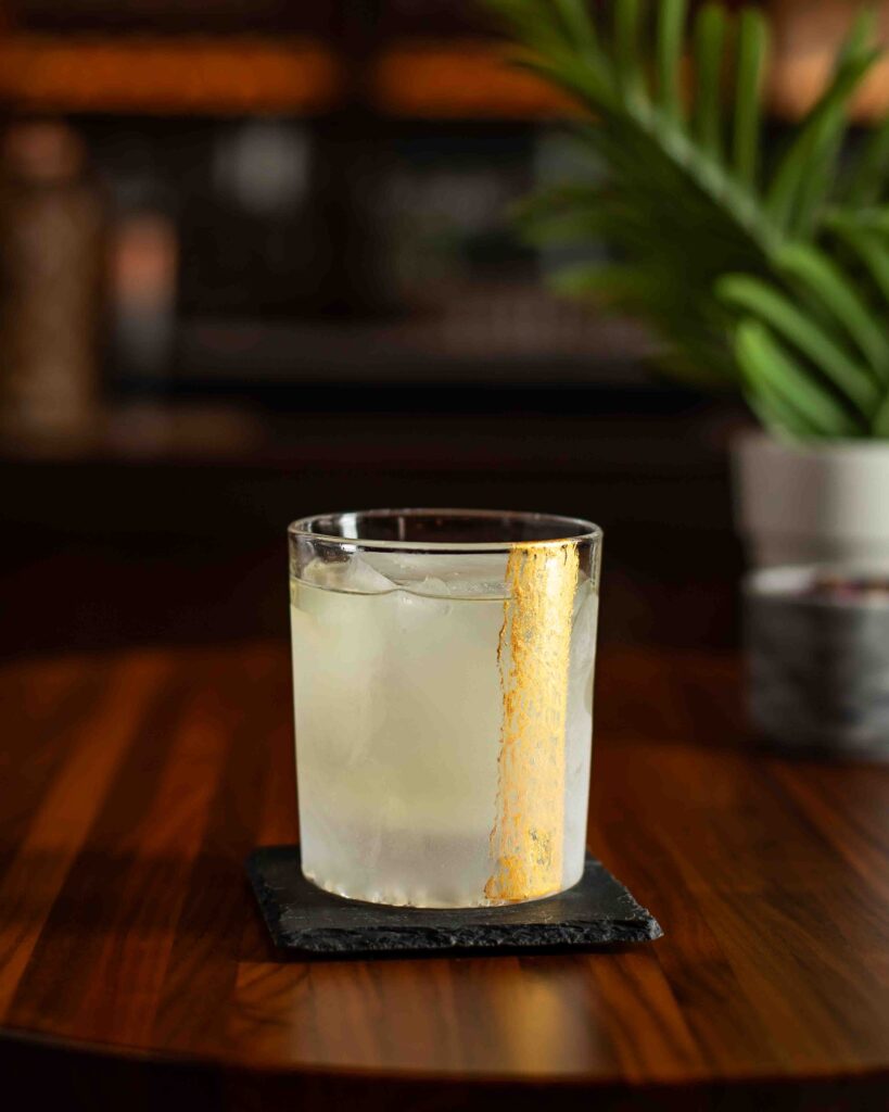 Clarified passion fruit cocktail served over ice in a clear rocks glass with a gold painted streak