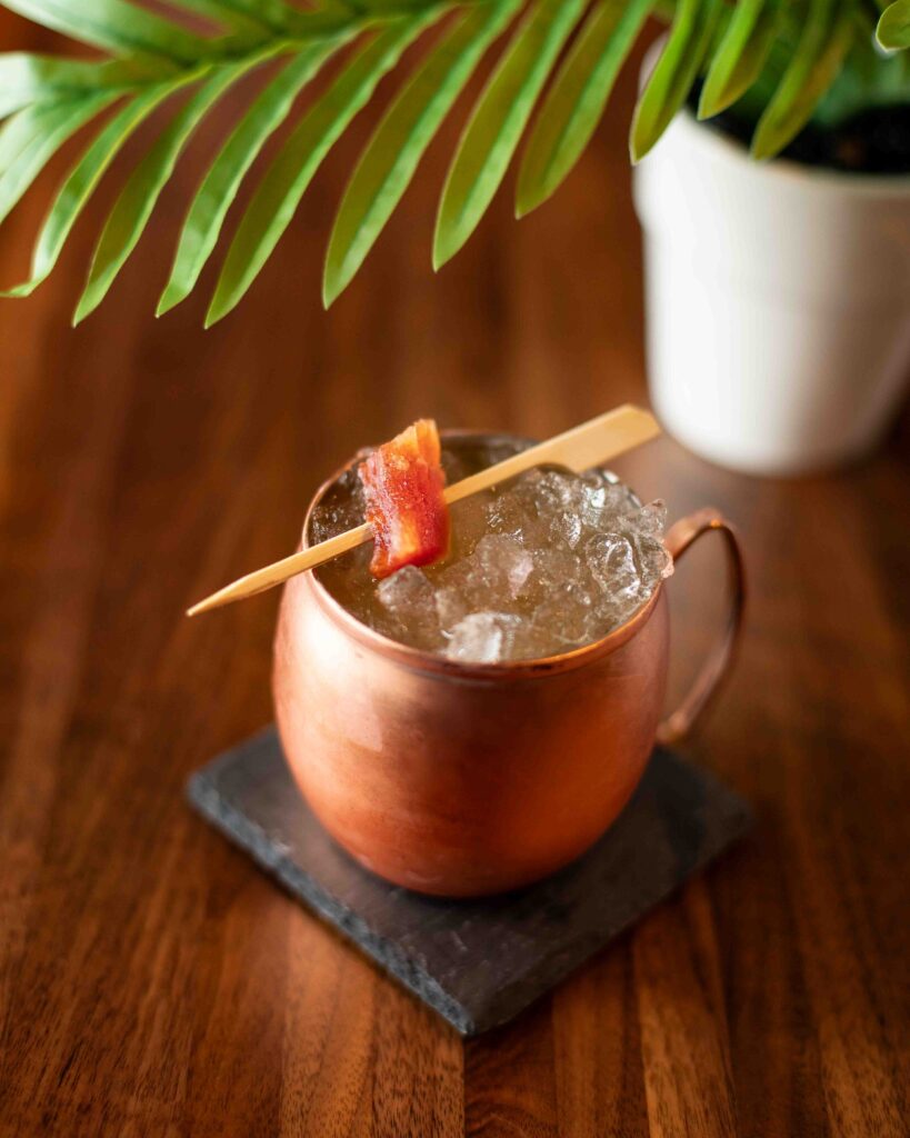 Papaya mule cocktail served over crushed ice in a copper mug, garnished with candied papaya on a cocktail pick.