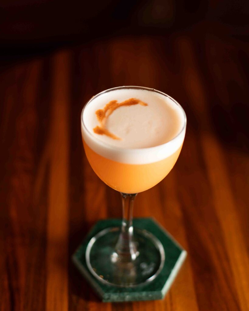 Passionfruit Hunny cocktail with a foamy top and bitters swirl, served in a coupe glass on a green hexagonal coaster.