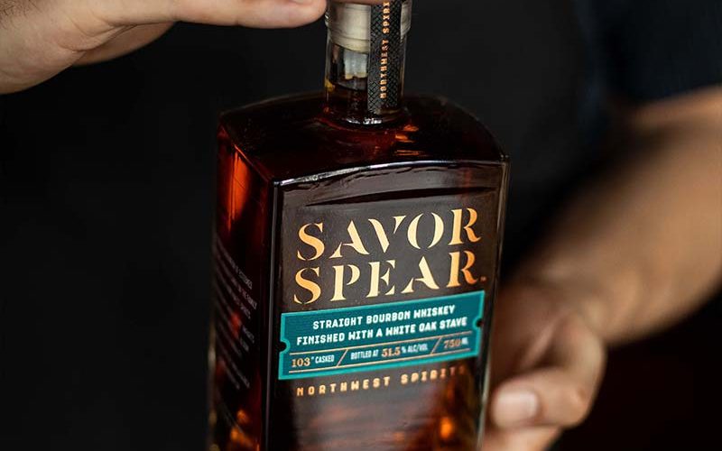 A man is holding a bottle of Savor Spear® Straight Bourbon Whiskey in his hands